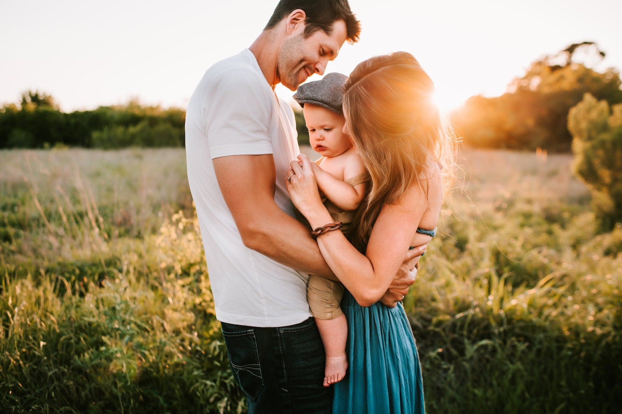 Young family of 3 with a father, mother and young baby at sunset in a field